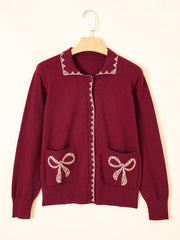 Burgundy knit cardigan with lace trimmed collar and bow pockets on a hanger
