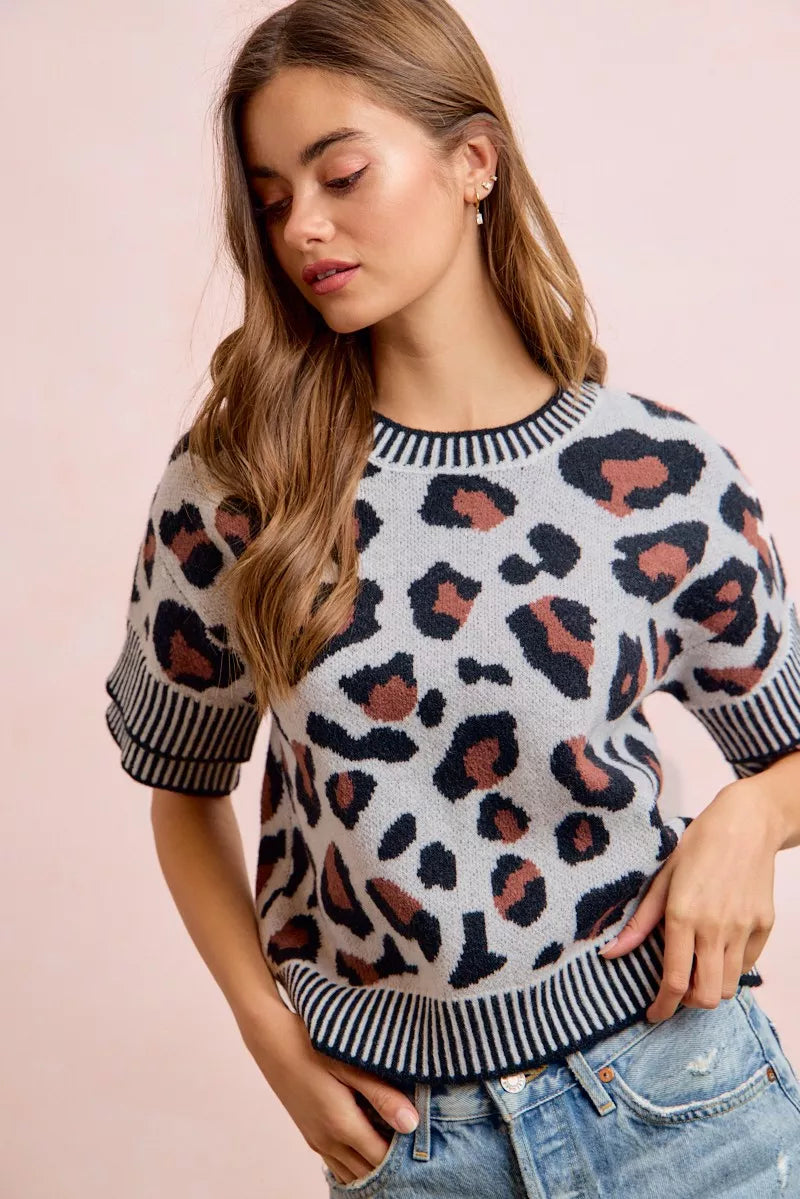 Front view of a light gray leopard print knit top, looking down with hands in pockets.