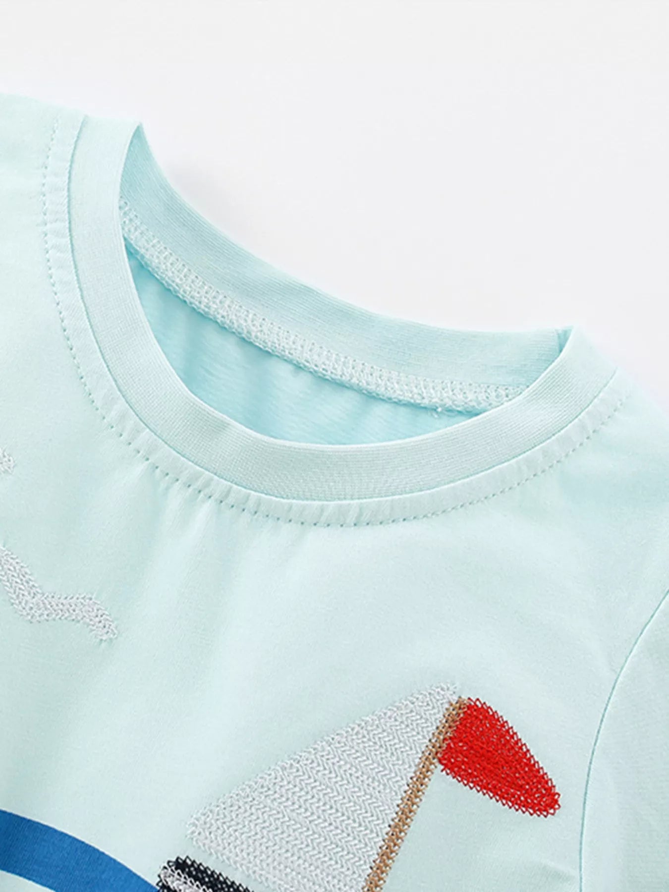 Close-up of the mint blue shirt neckline and the embroidered white sail with red flag