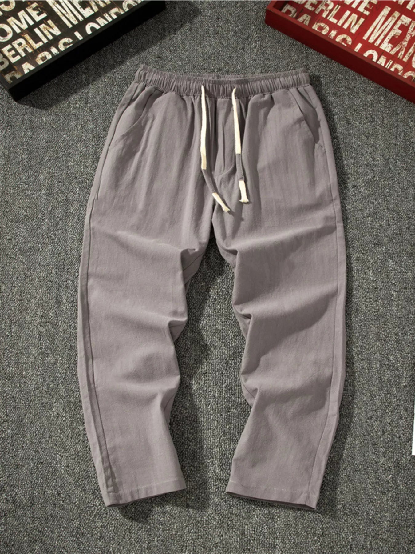 Men's light gray loose-fit pants with a drawstring waist and pockets.