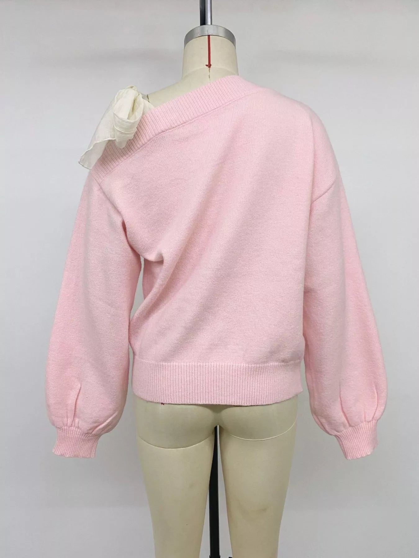 Back view of a pink one-shoulder sweater with a cream bow on a mannequin