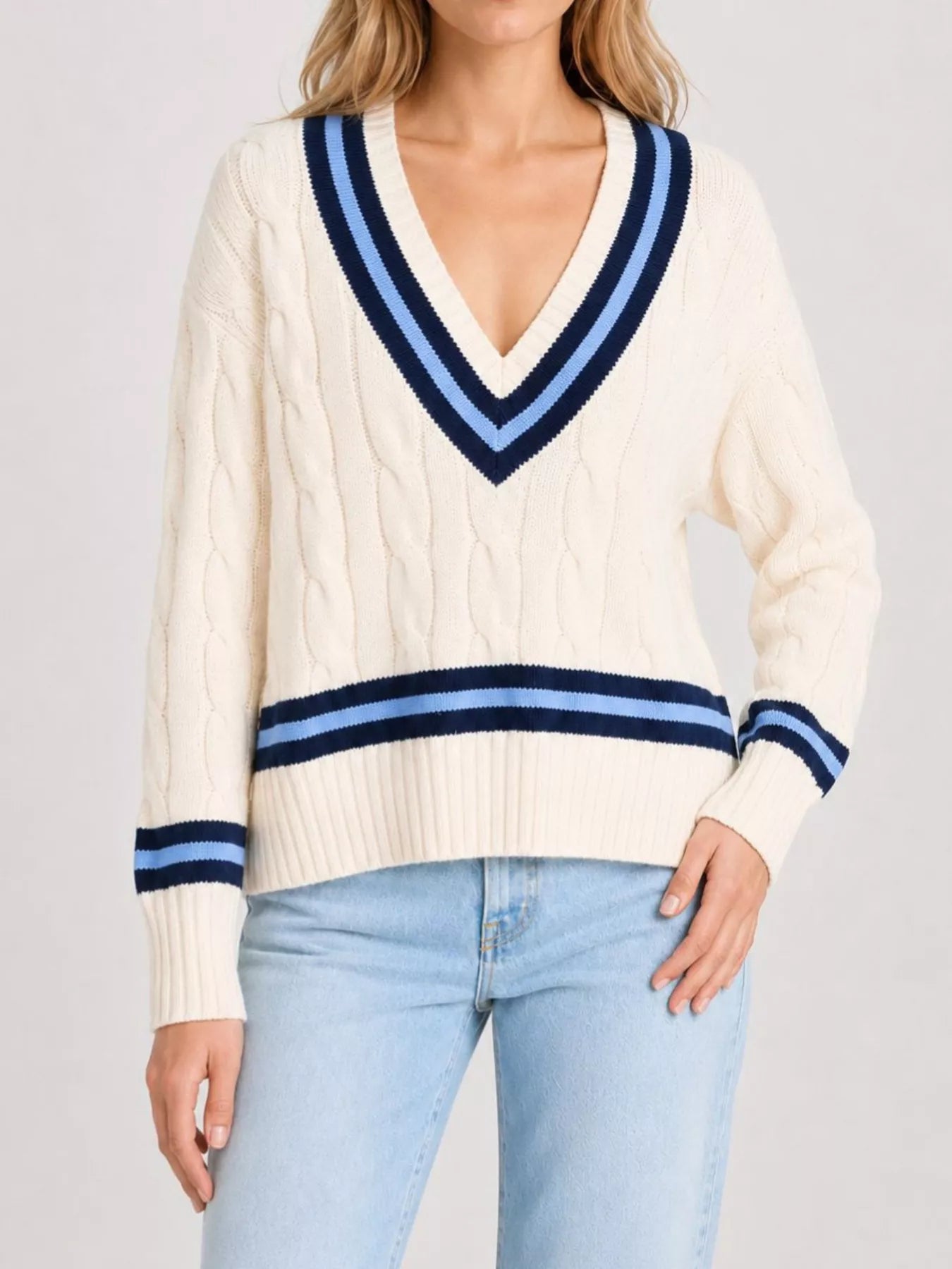On-model front view of a cream cable knit sweater with navy striped trim, hand on hip