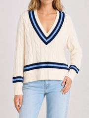On-model front view of a cream cable knit sweater with navy striped trim, hand on hip