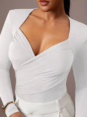 Close cropped front view of white ruched surplice bodysuit paired with white trousers