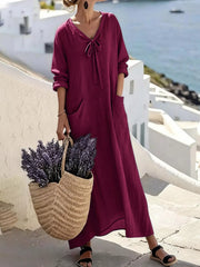 Model wearing plum purple long sleeve loose maxi dress outdoors, full view with large pockets and tie neck