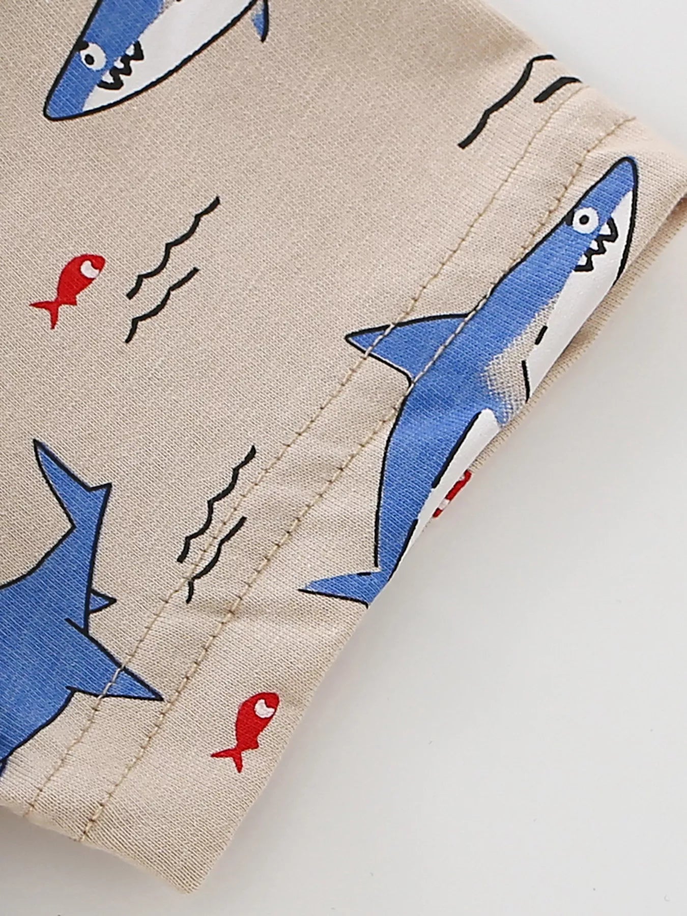 Close-up of sleeve hem stitching and shark print detail on tan children's tee