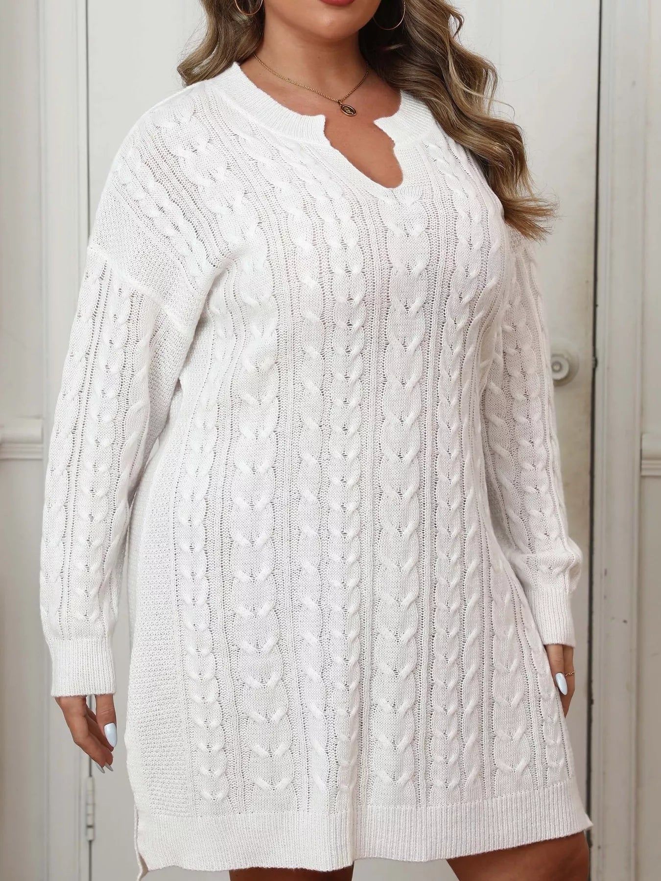 Side view of white cable knit sweater dress with long sleeves and side slit