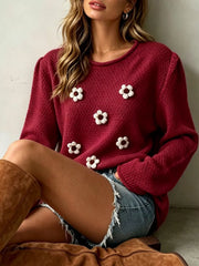 Seated close view of a burgundy textured knit sweater with white floral appliques