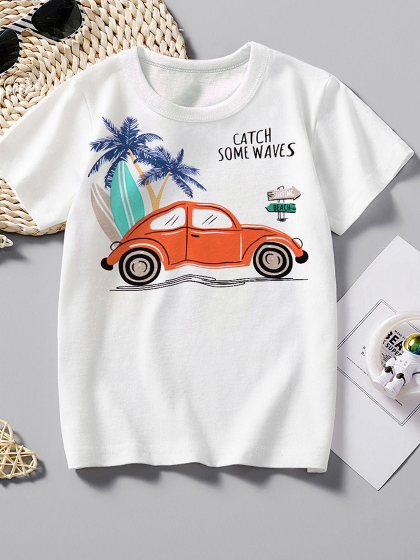 Flat lay front view of white children's T-shirt with an orange car, palm trees and surfboards