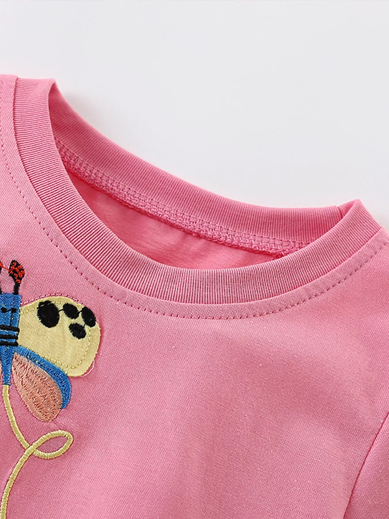 Close-up of the pink shirt neckline and the embroidered yellow and blue butterfly nearby