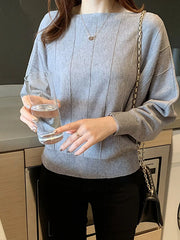 Front view of the gray batwing sleeve knit top with vertical seams, holding a glass indoors.