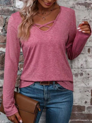 Pink long-sleeve T-shirt with crisscross V-neck detail, shown styled with jeans and a brown clutch.