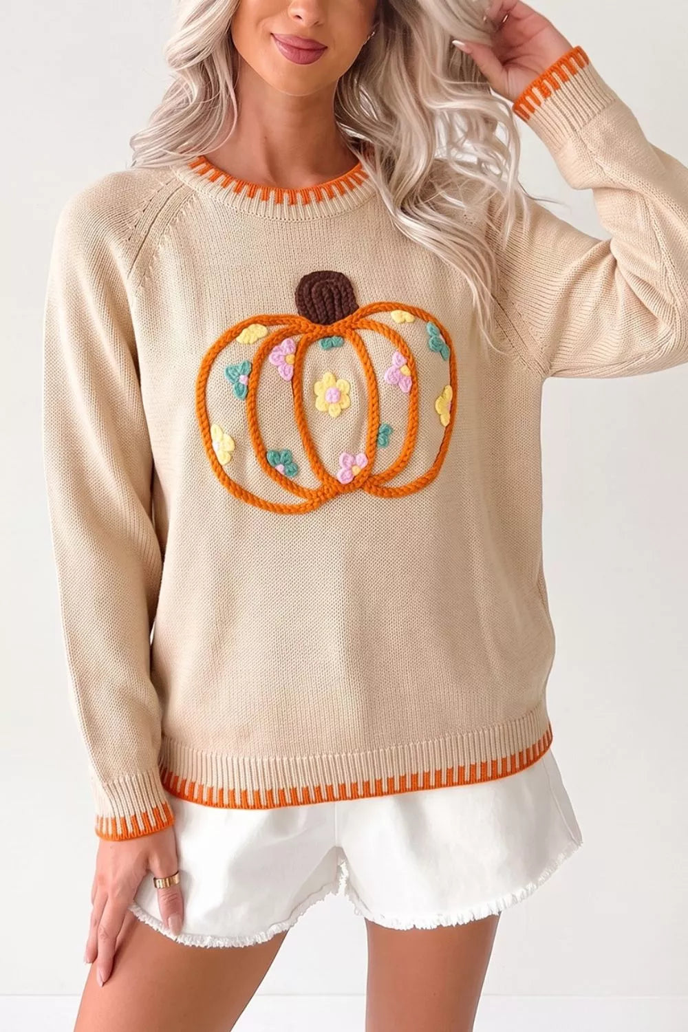 Front view of a beige pumpkin sweater with orange trim at the neckline, cuffs, and hem