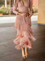 Lower view of a pink fringed maxi dress showing the tiered fringe skirt and gold clutch