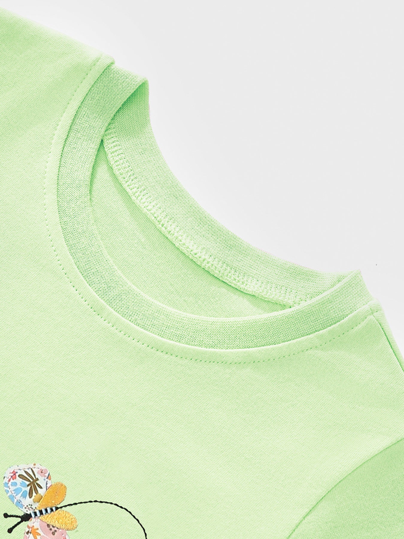 Close-up detail of the light green round neckline and butterfly appliqué on children's tee