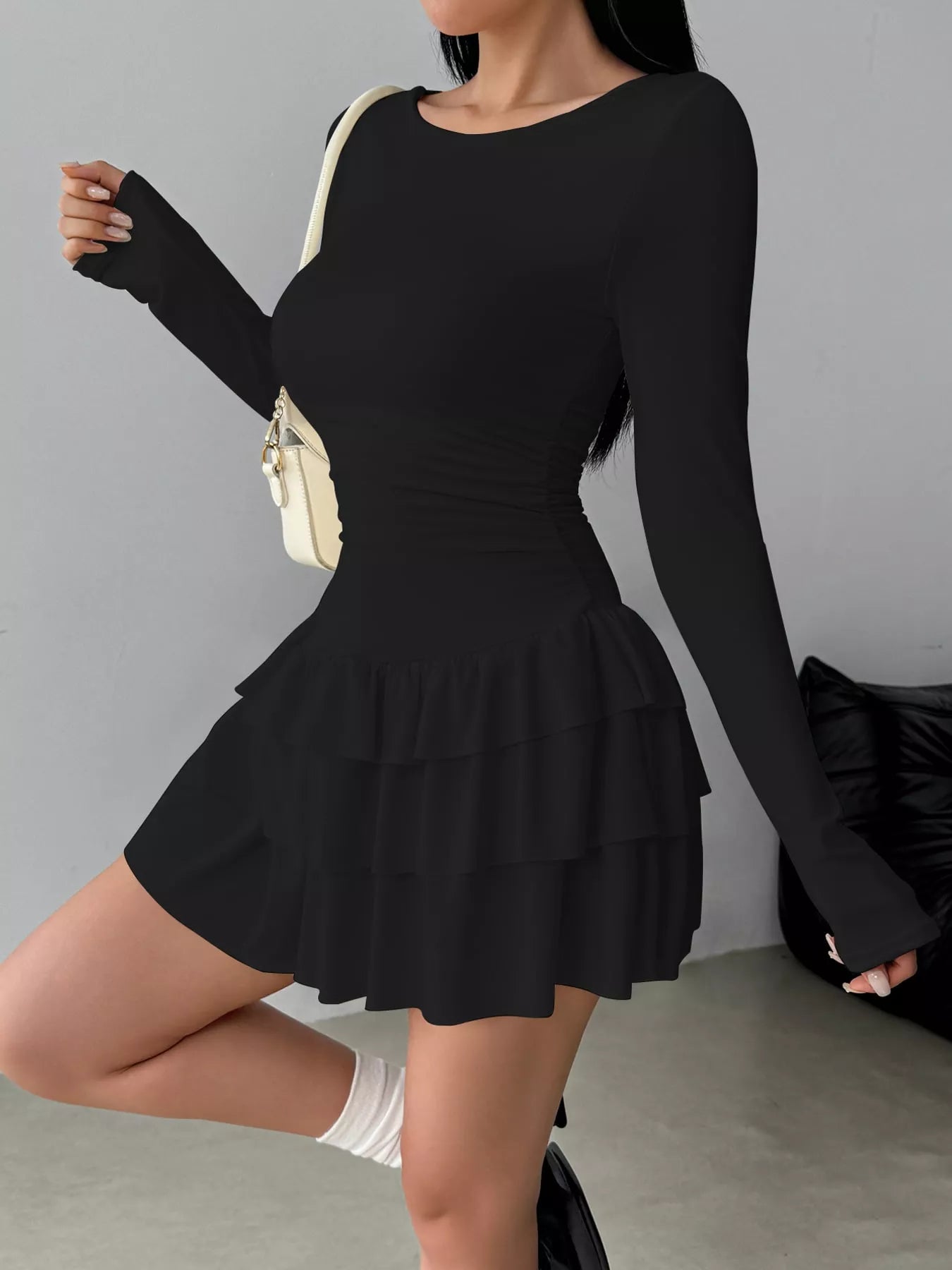 Black long sleeve mini dress worn in a side view showing the ruched waist and tiered ruffle skirt