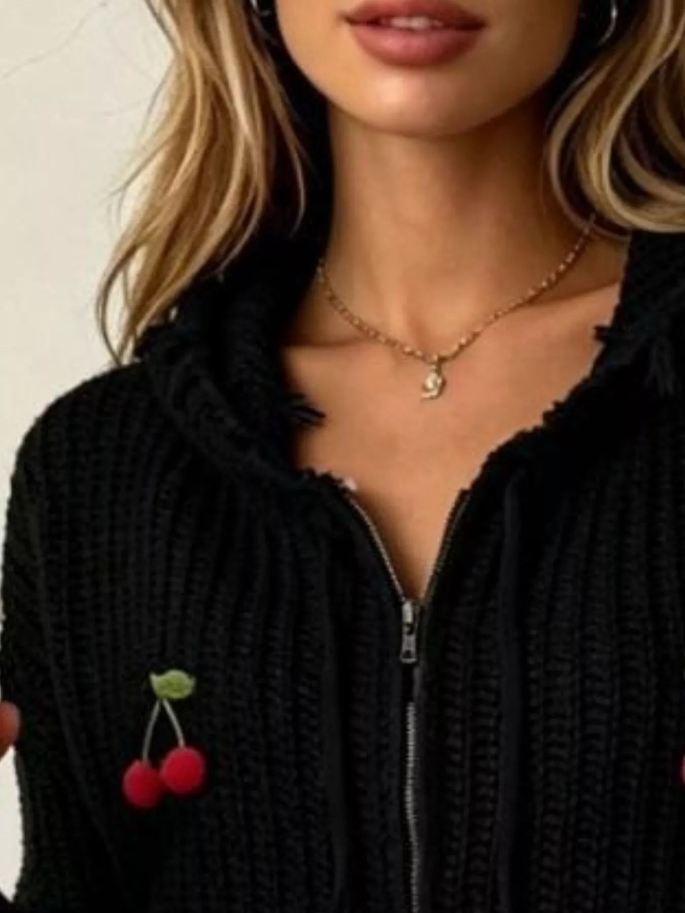 Close up of black knit zip up hooded sweater showing zipper and red cherry applique detail
