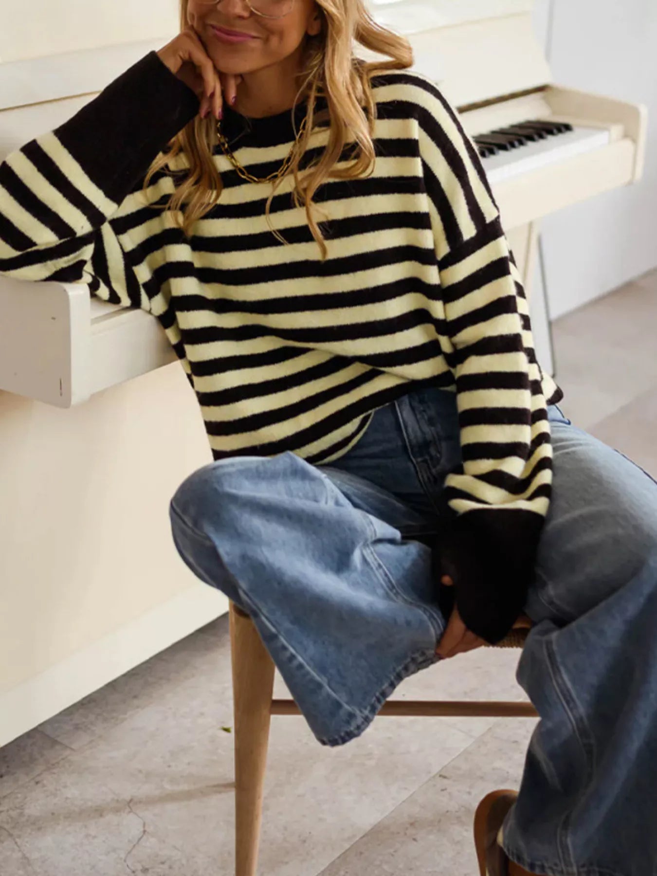 Seated on-model front view of a black and yellow striped crew neck sweater