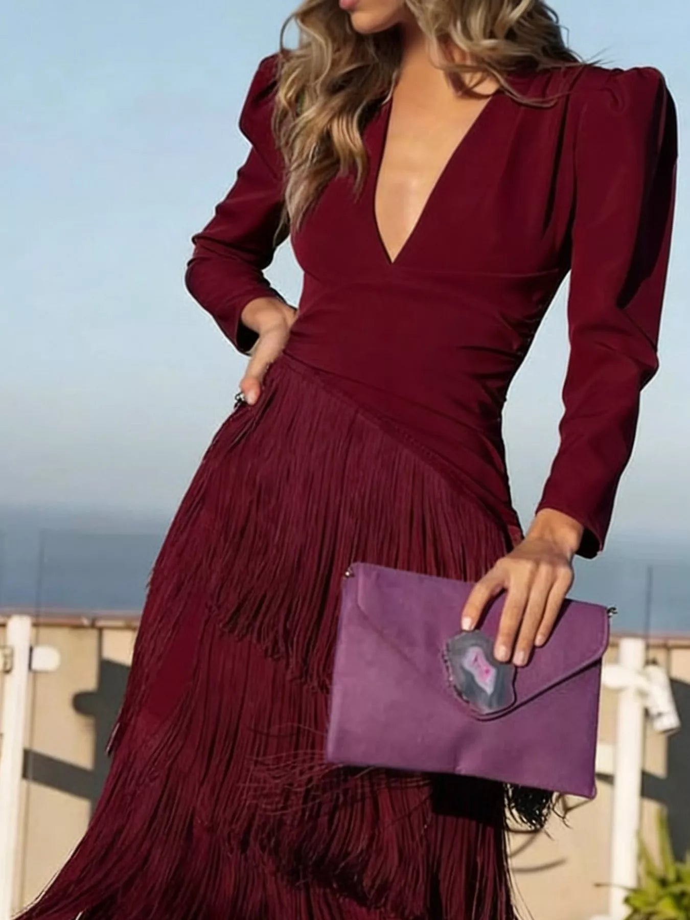 Close front view of a burgundy fringed maxi dress with a tiered fringe skirt