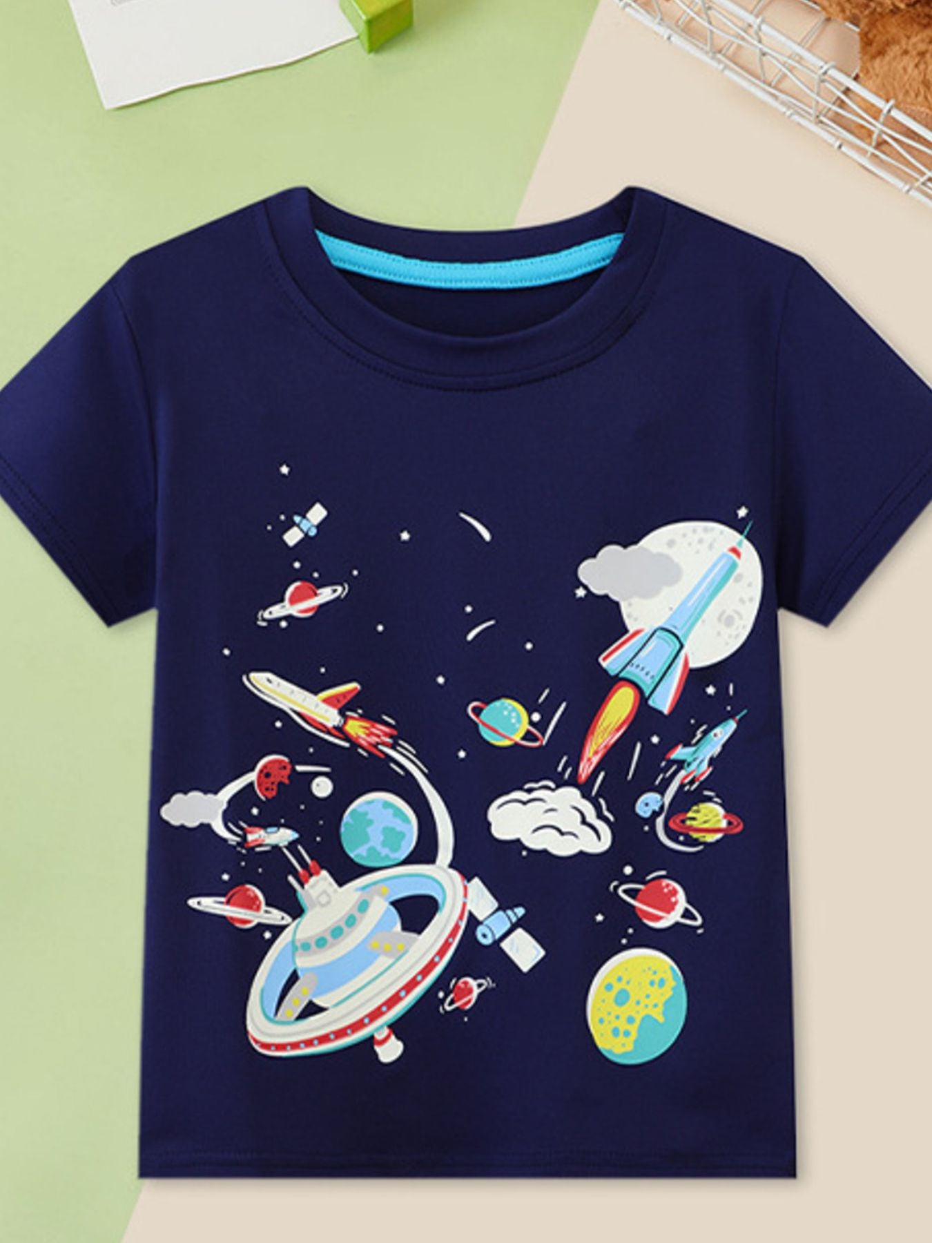 Flat front view of a navy children's tee with rockets, planets, a space station and stars