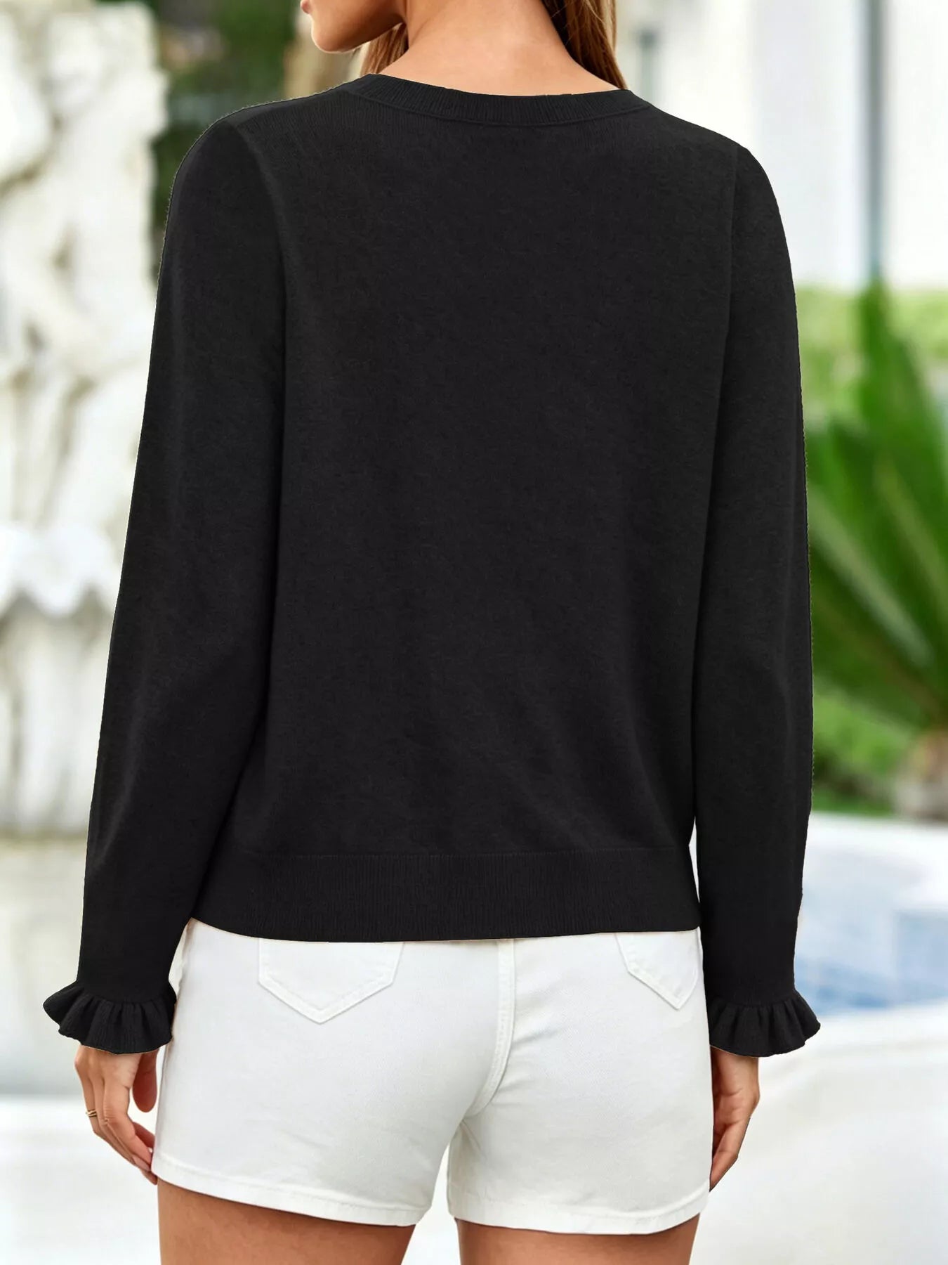 Back view of black ruffle trimmed knit cardigan with ruffled cuffs and white shorts