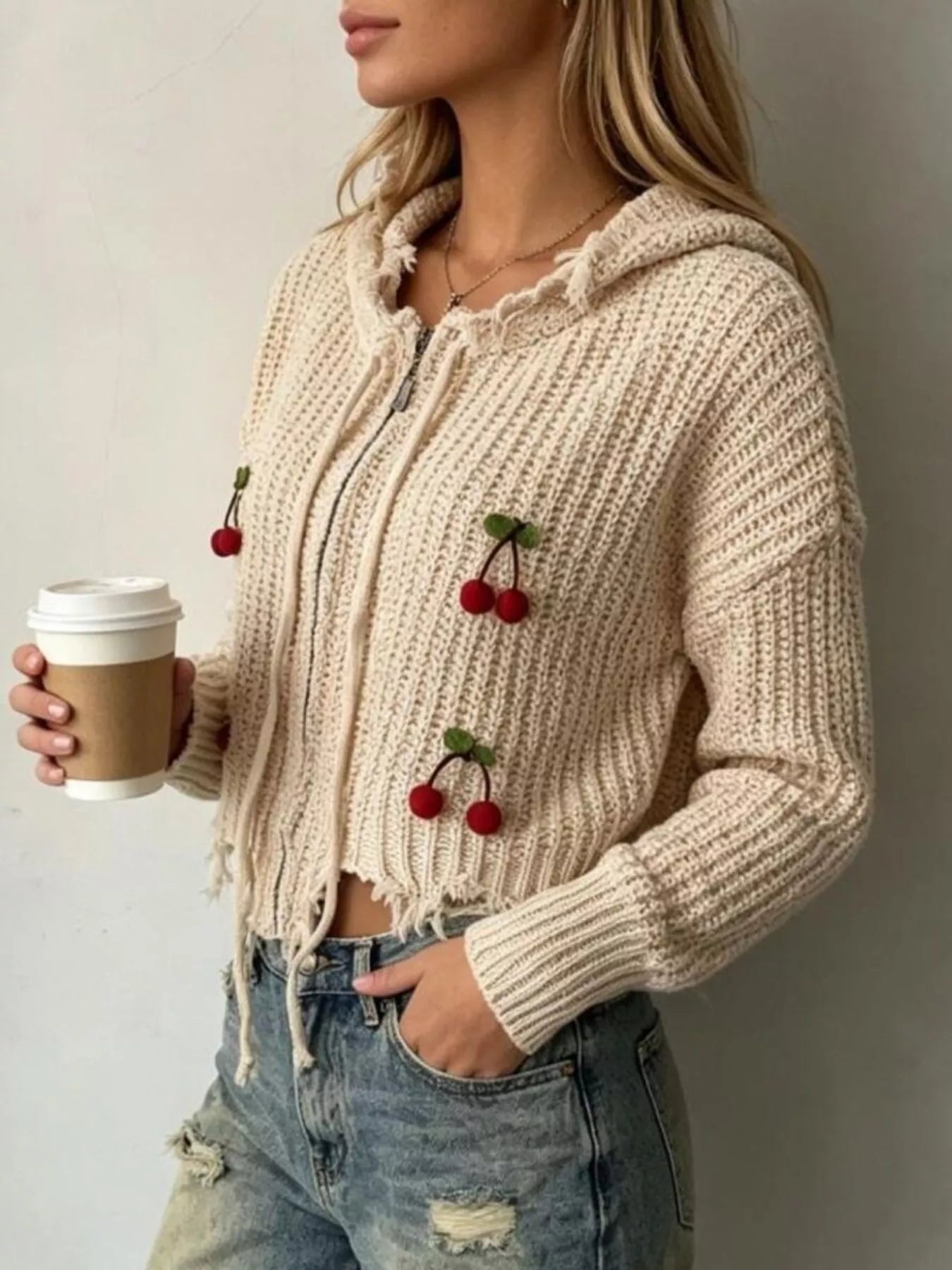 Side view of apricot knit zip up hooded sweater with red cherry appliques and frayed hem