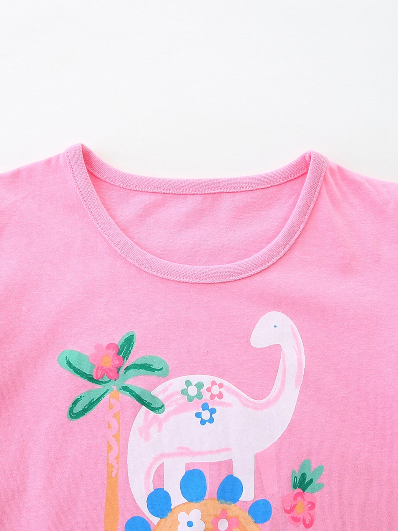 Close up of pink children's t-shirt round neckline with white dinosaur and palm tree print