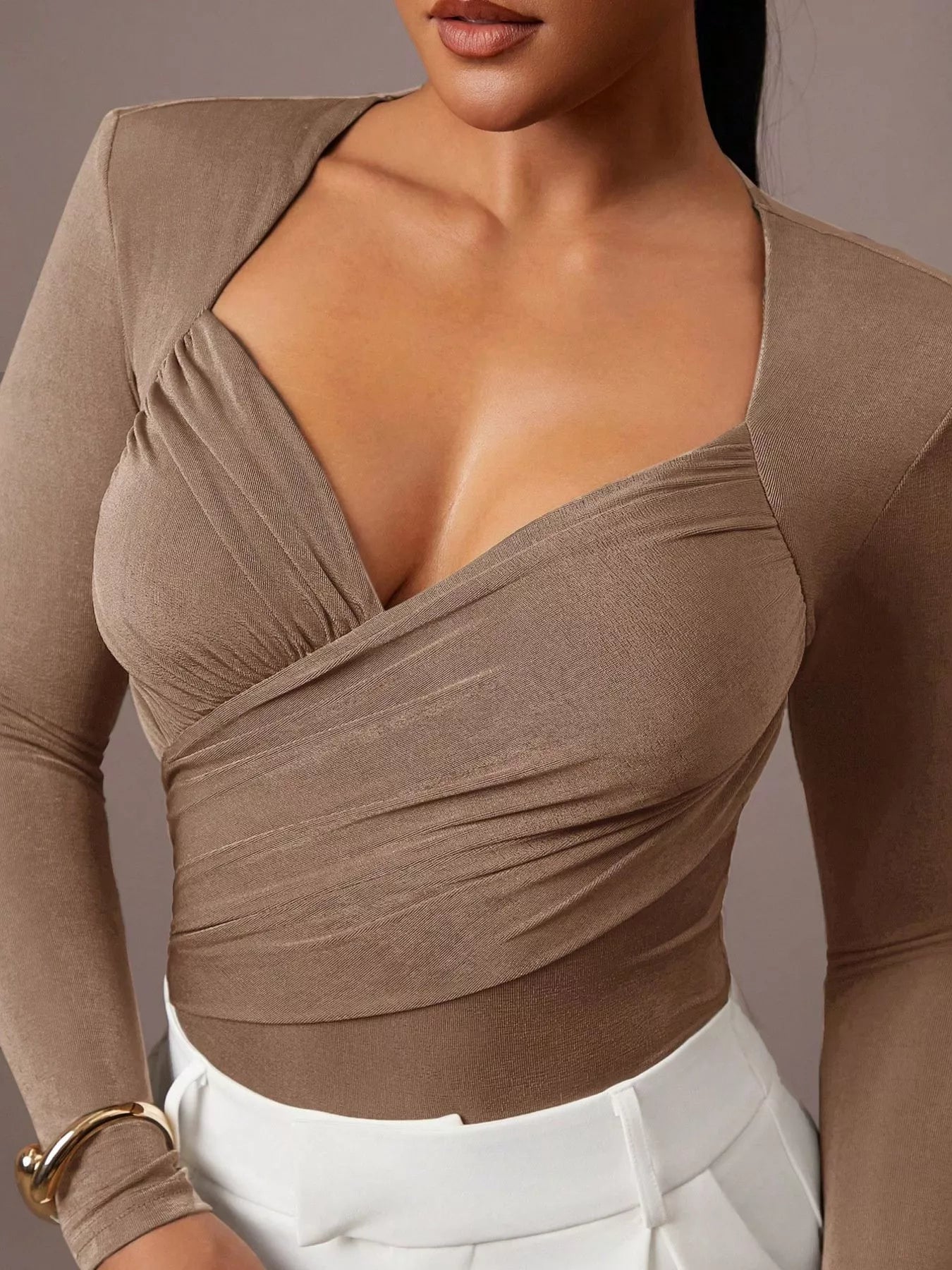 Close cropped front view of khaki ruched surplice bodysuit paired with white trousers