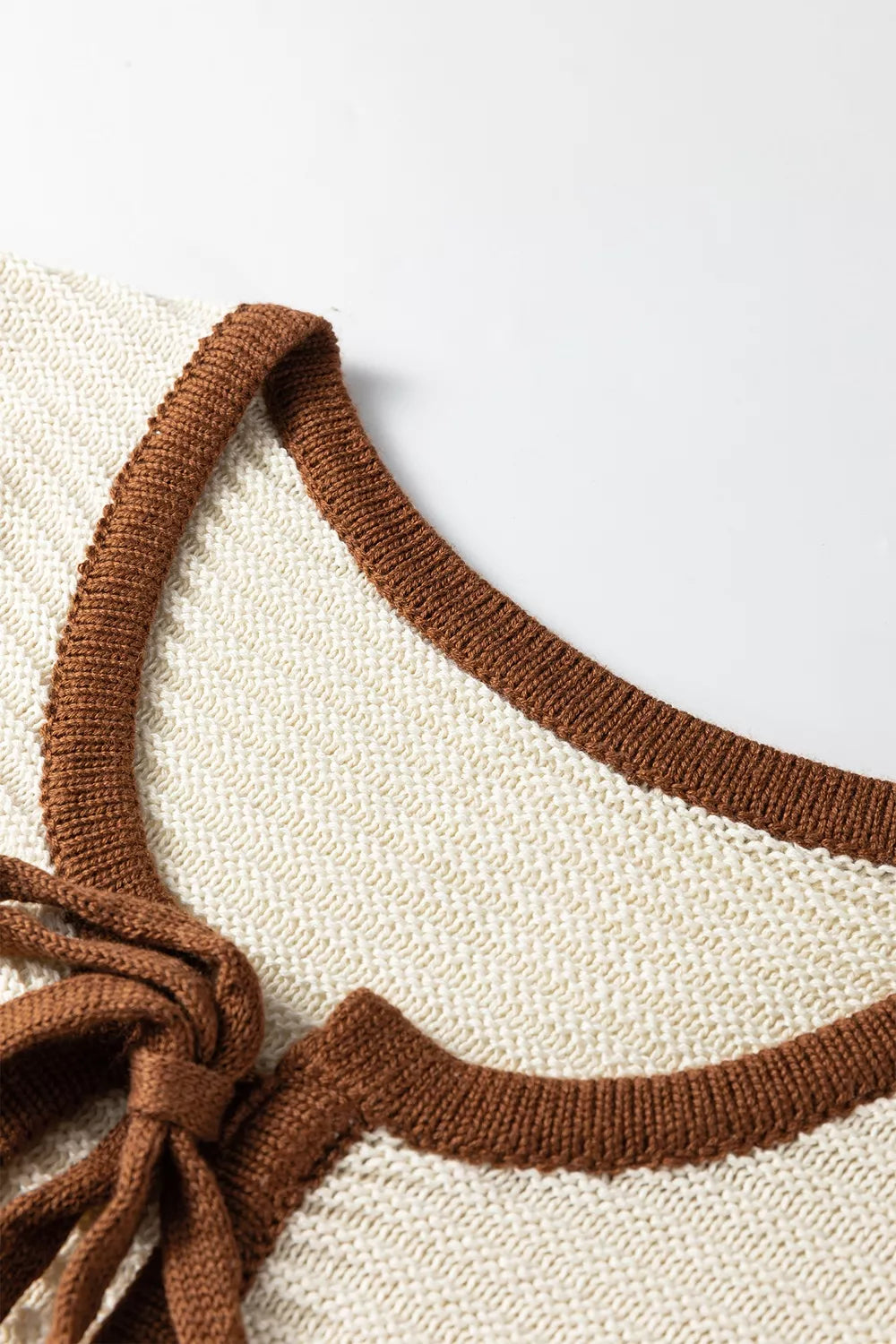 Close up front detail of a beige sweater vest neckline with brown contrast trim