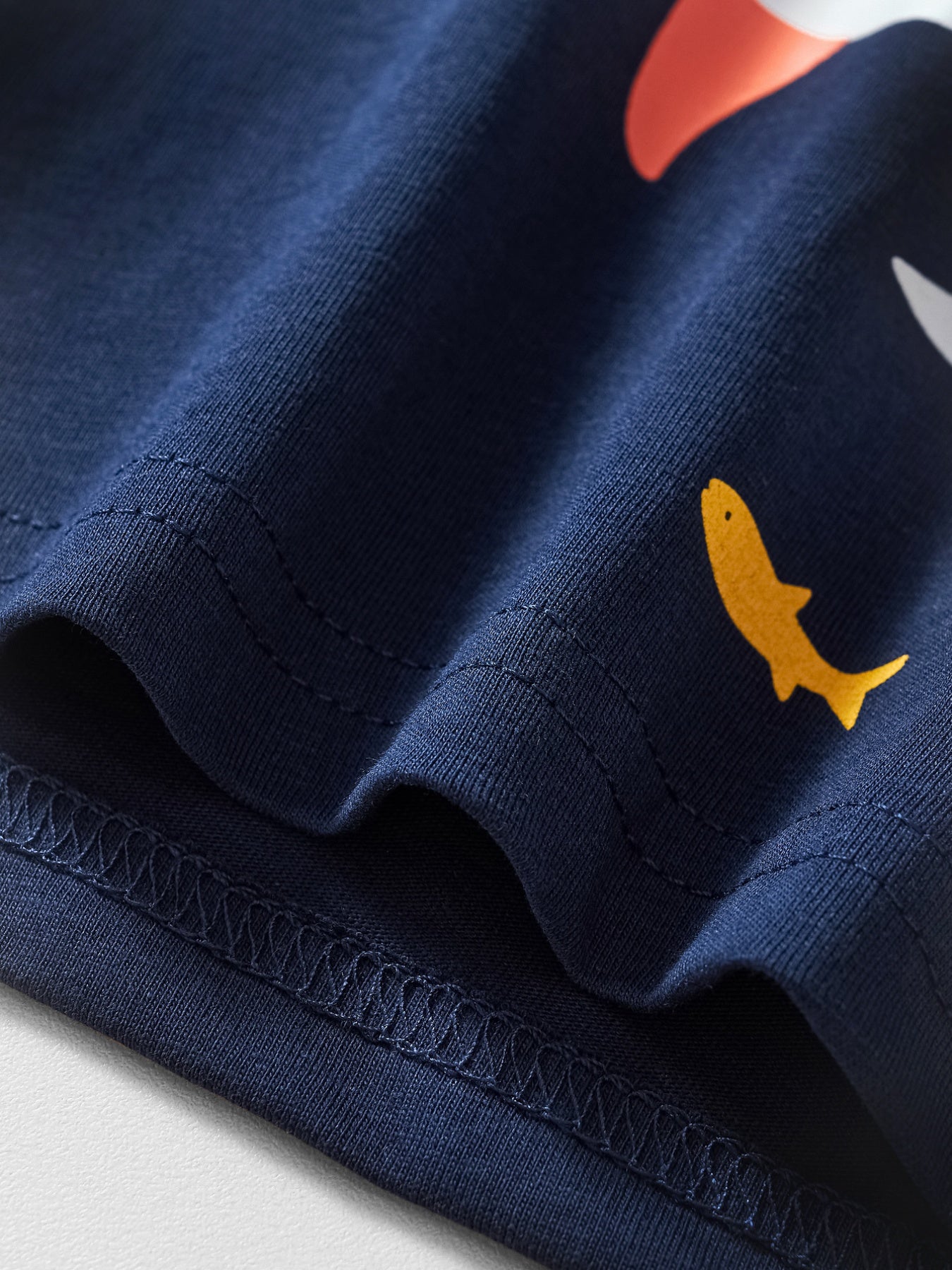 Close view of the hem stitching and small yellow fish on the dark navy children's t-shirt
