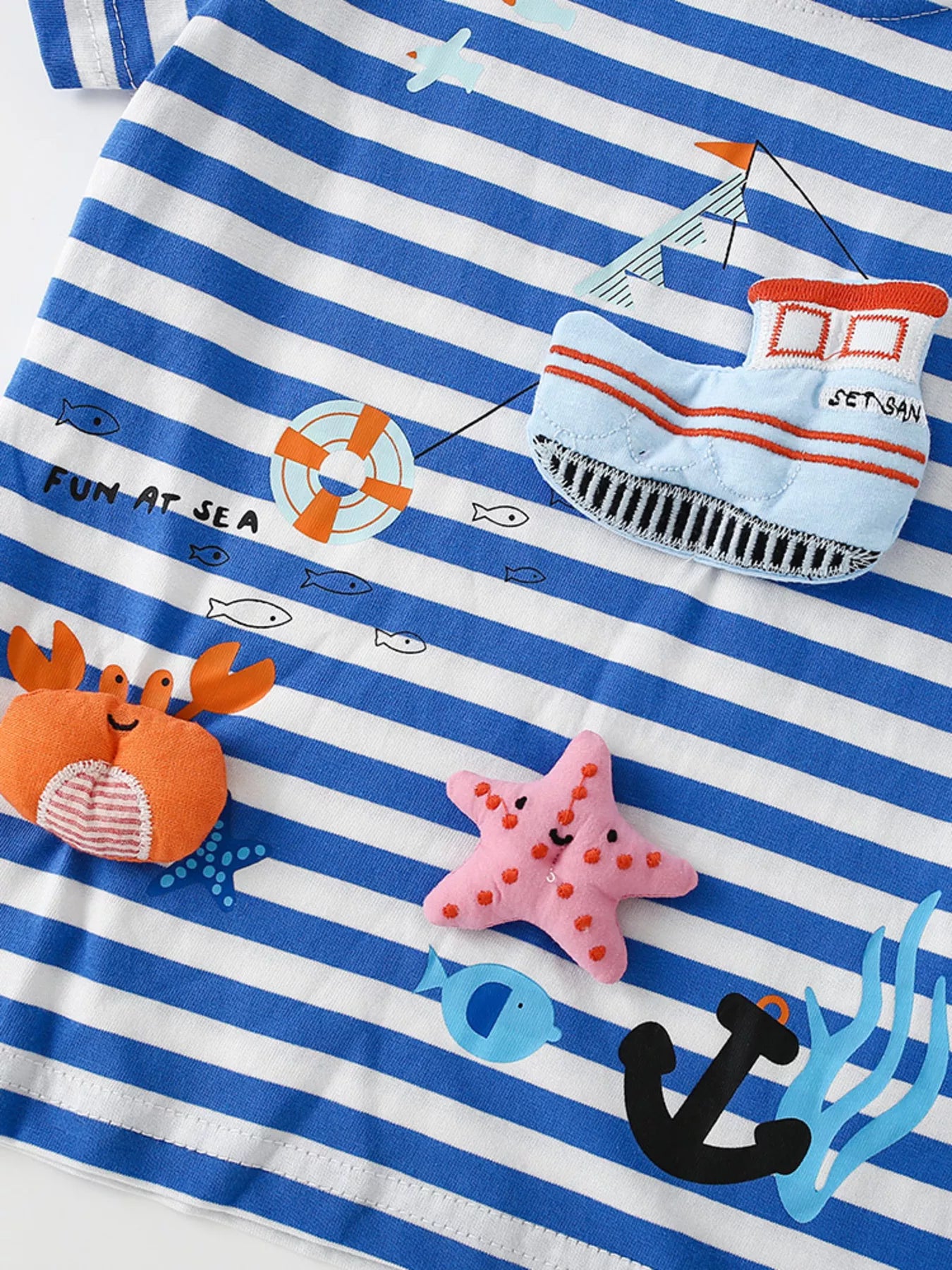 Close up of the nautical appliques on a children's blue and white striped short sleeve tee