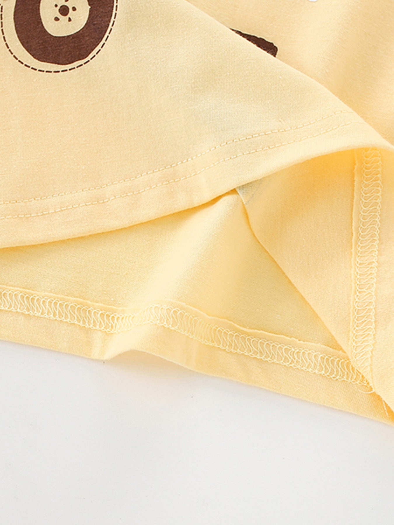 Close-up of the hem stitching and inner fabric on a pastel yellow children's lion graphic T-shirt