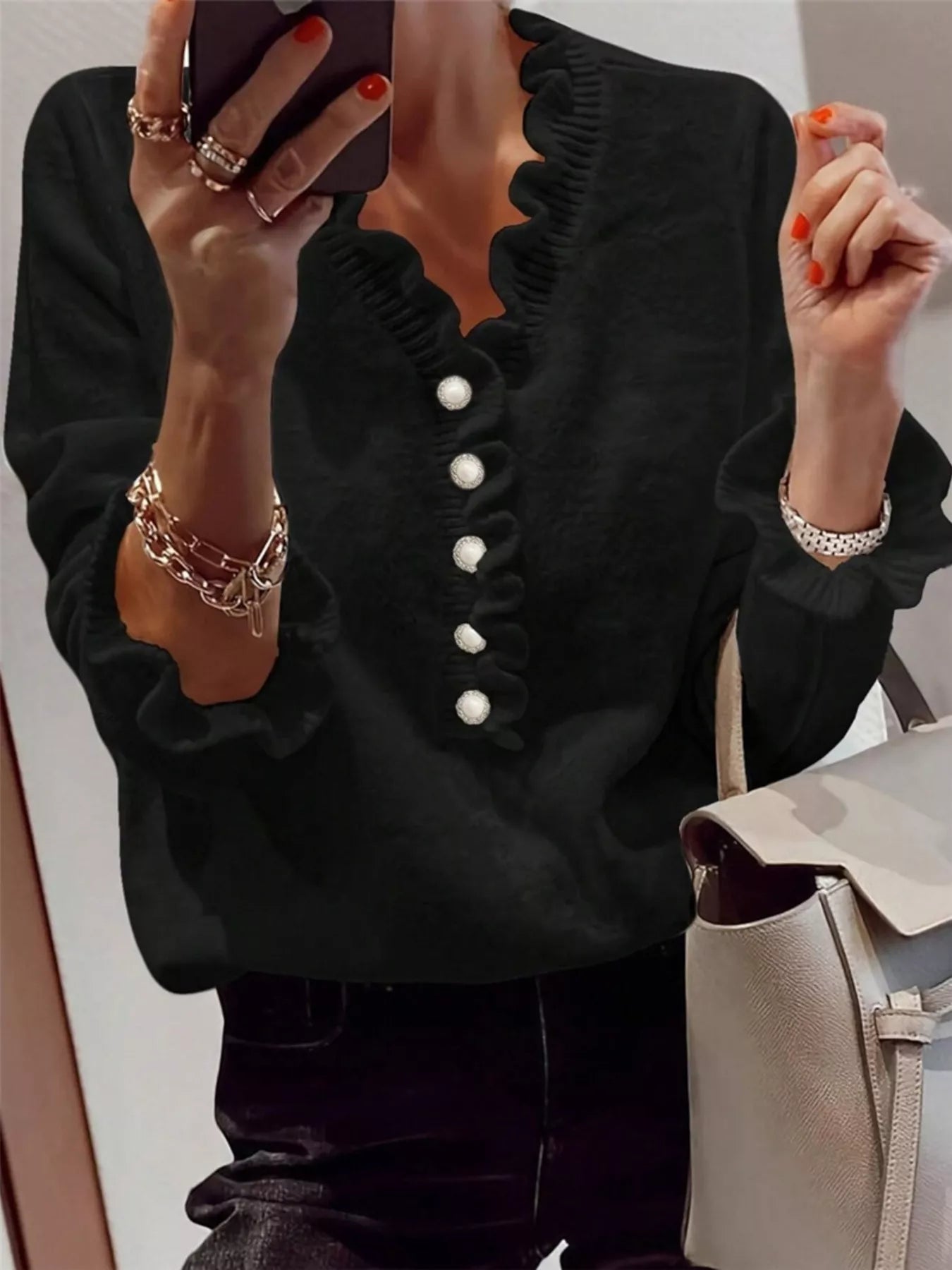 Mirror front view of a black ruffled sweater with pearl buttons and ruffled cuffs