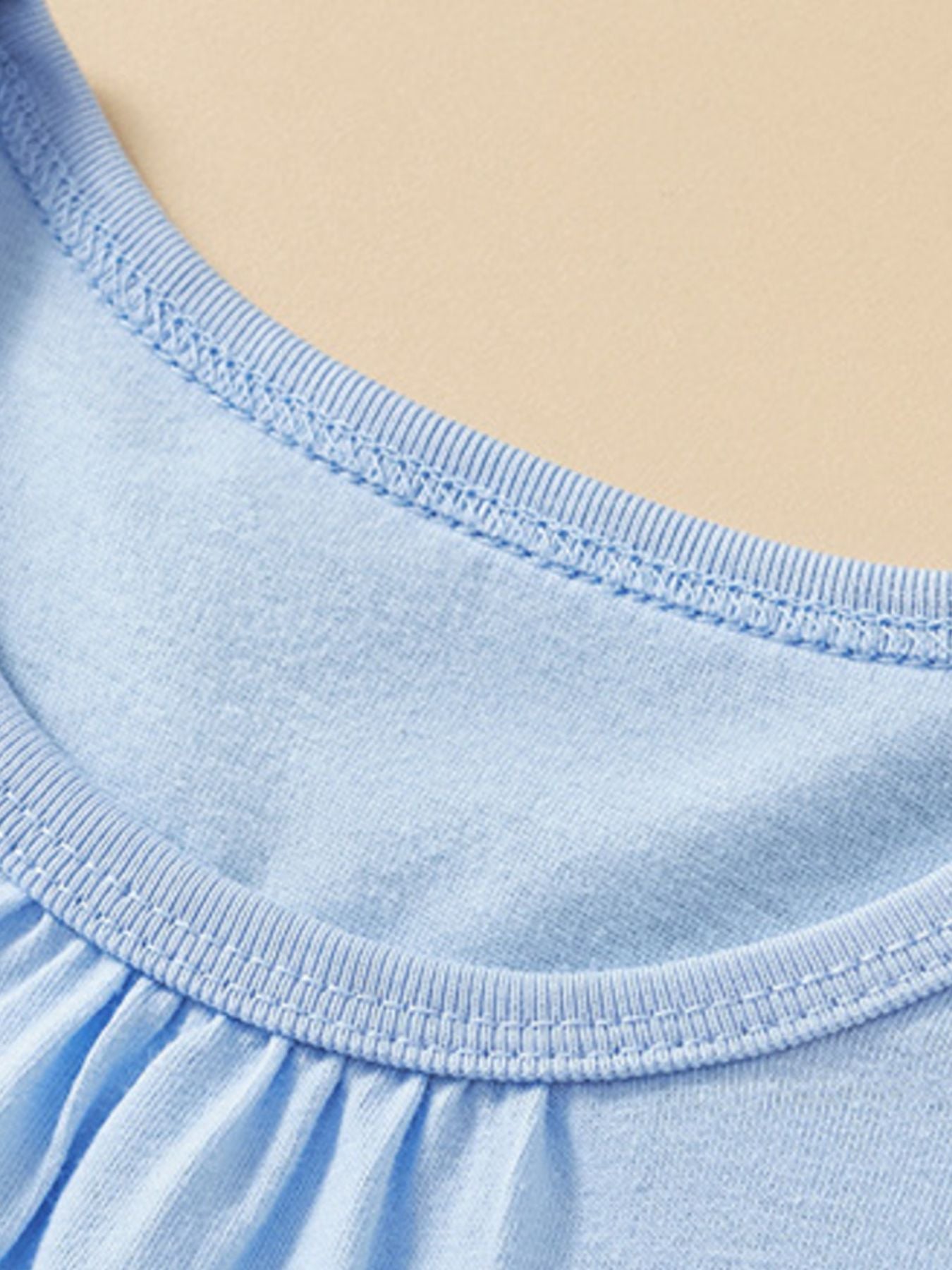 Close-up of the ribbed round neckline and gathered front on a pastel blue children's tee