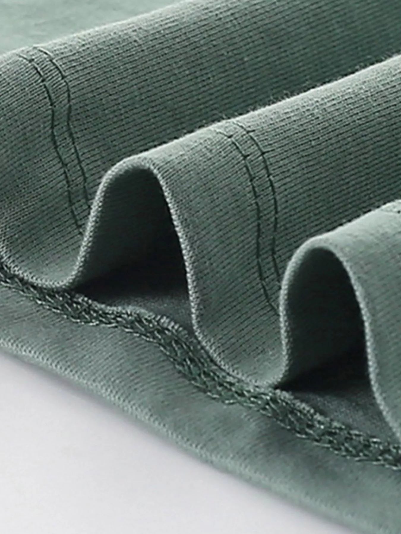 Close-up of the sage shirt hem showing double stitching and soft folded fabric