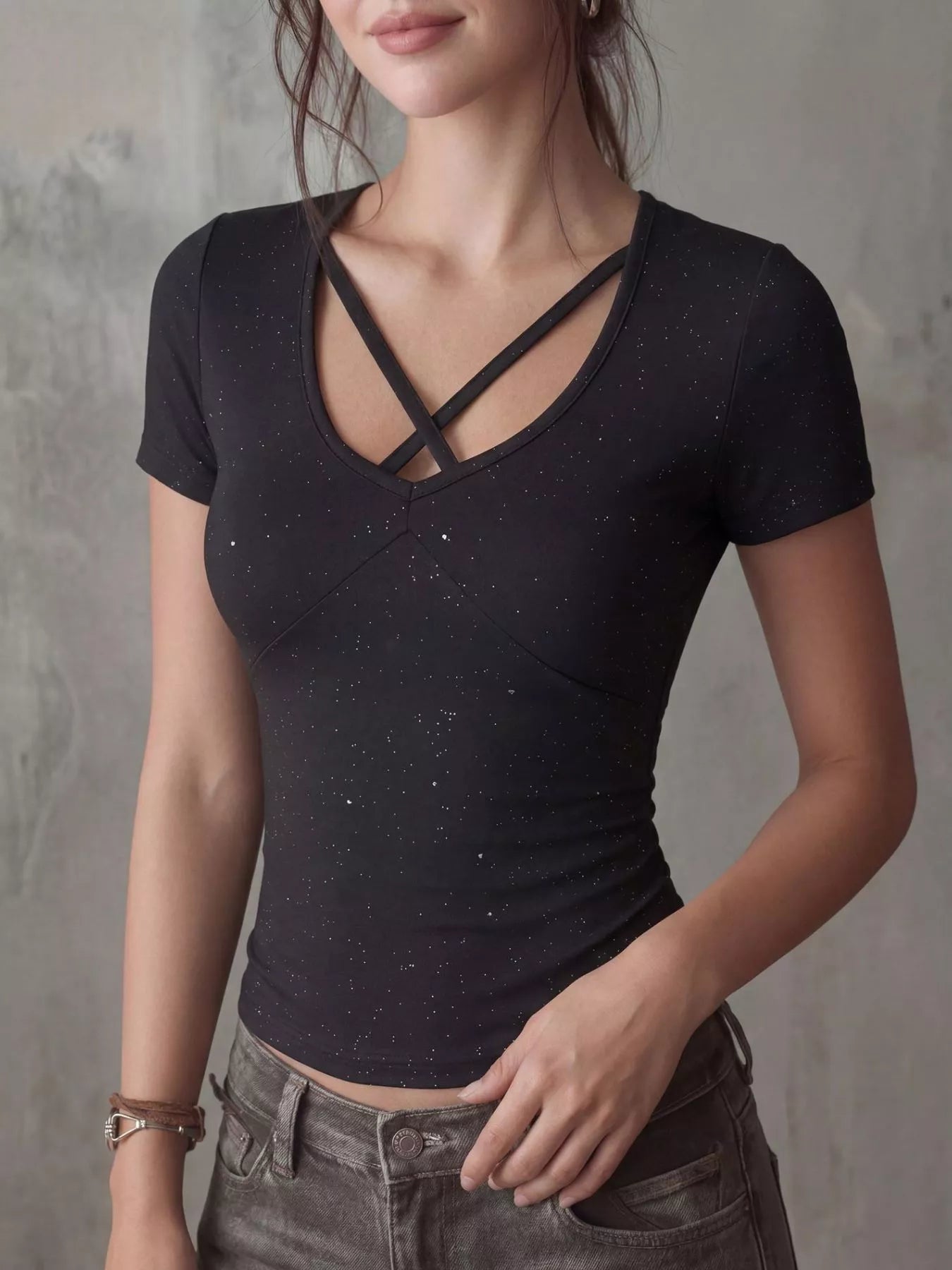 Close-up front view of a black fitted short-sleeve T-shirt with crossover neckline and speckled pattern