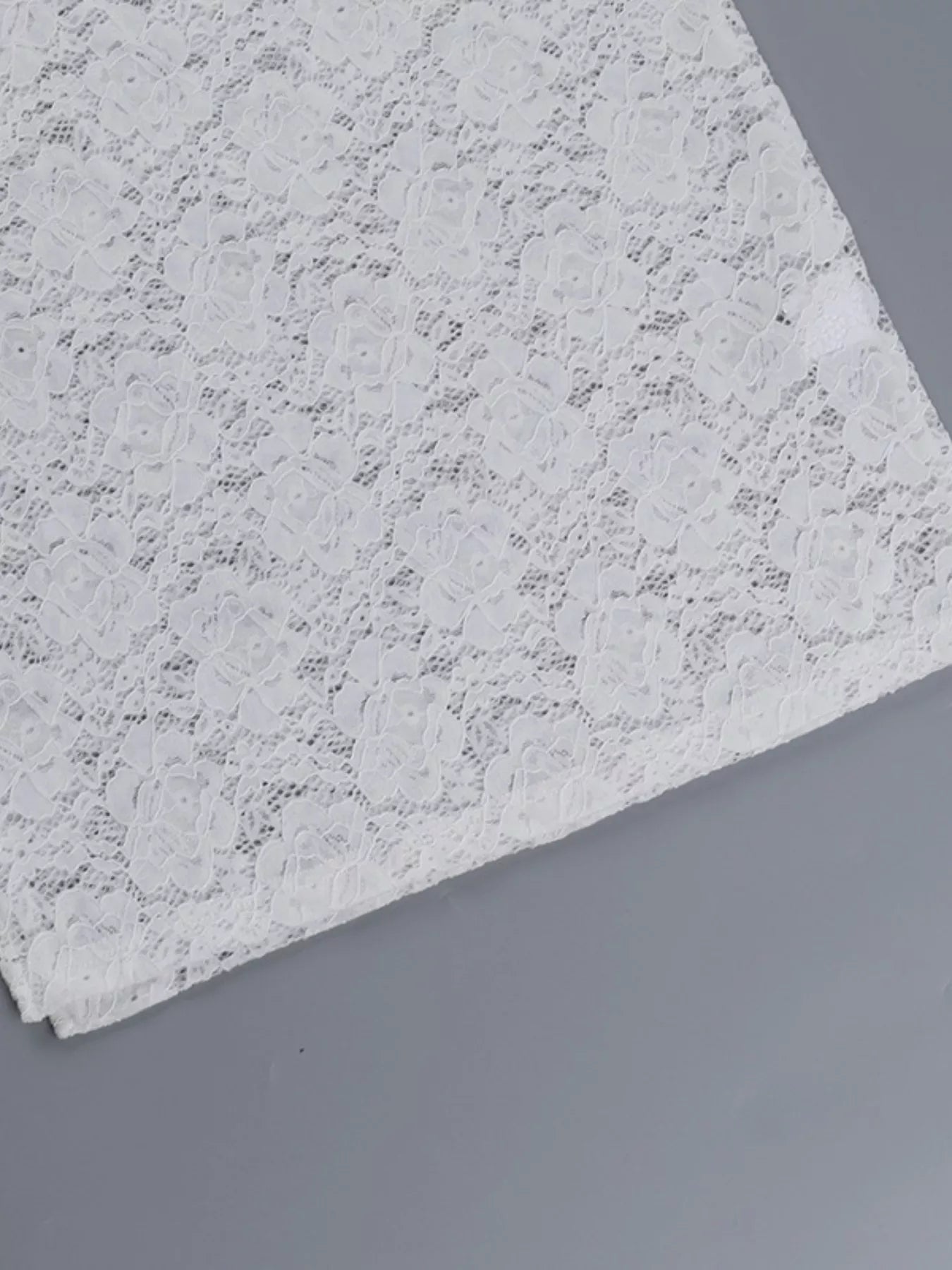 Flat detail of a white lace maxi dress skirt hem showing the floral lace pattern
