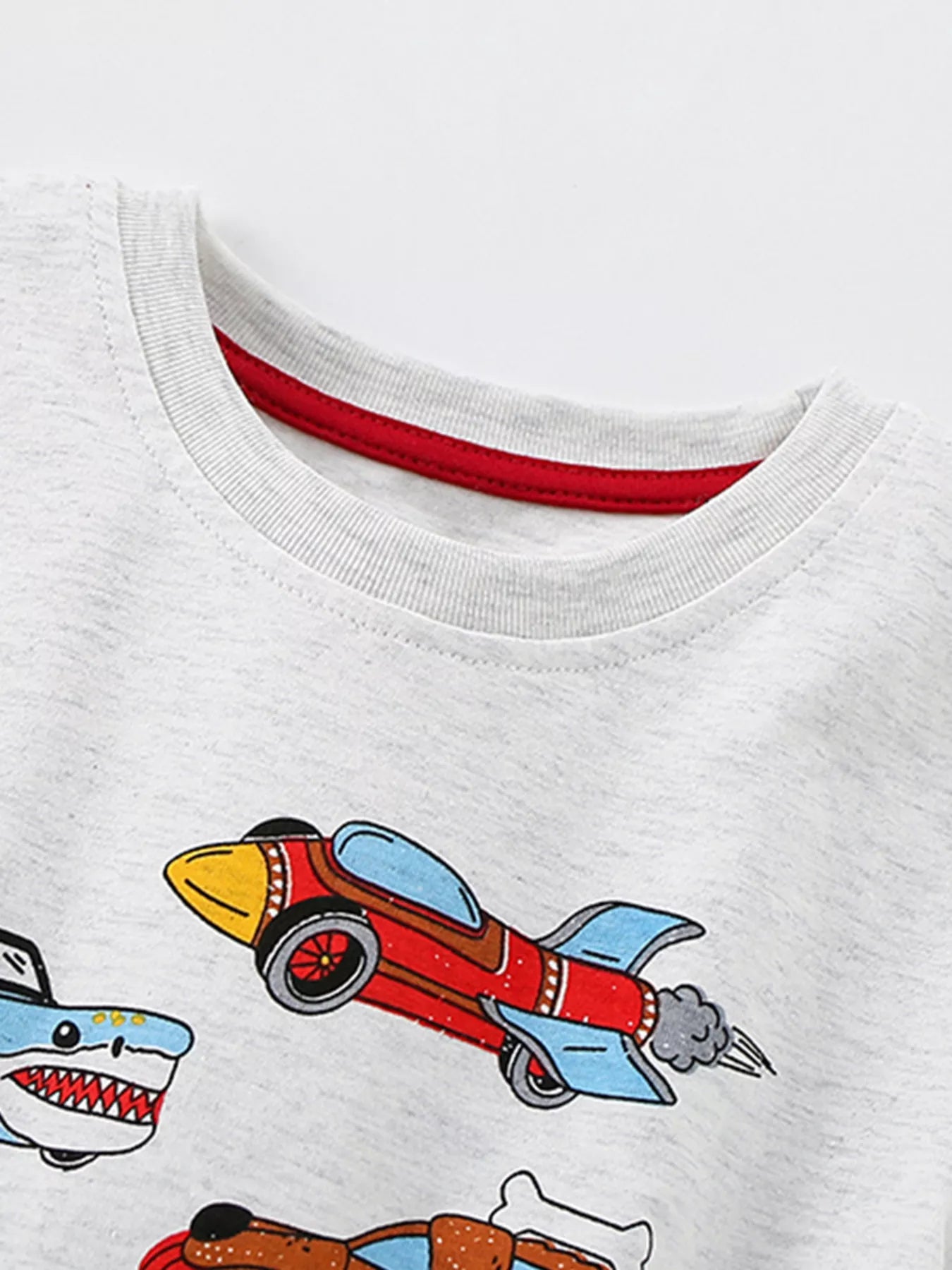 Close-up of the light gray crew neckline with red inner trim above a red rocket car print