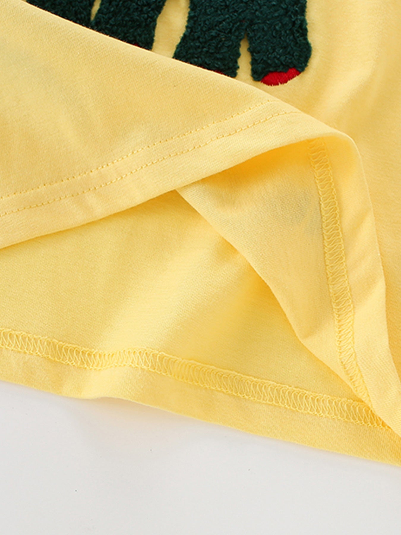 Close-up of the hem stitching and inner fabric on a yellow children's dinosaur graphic T-shirt
