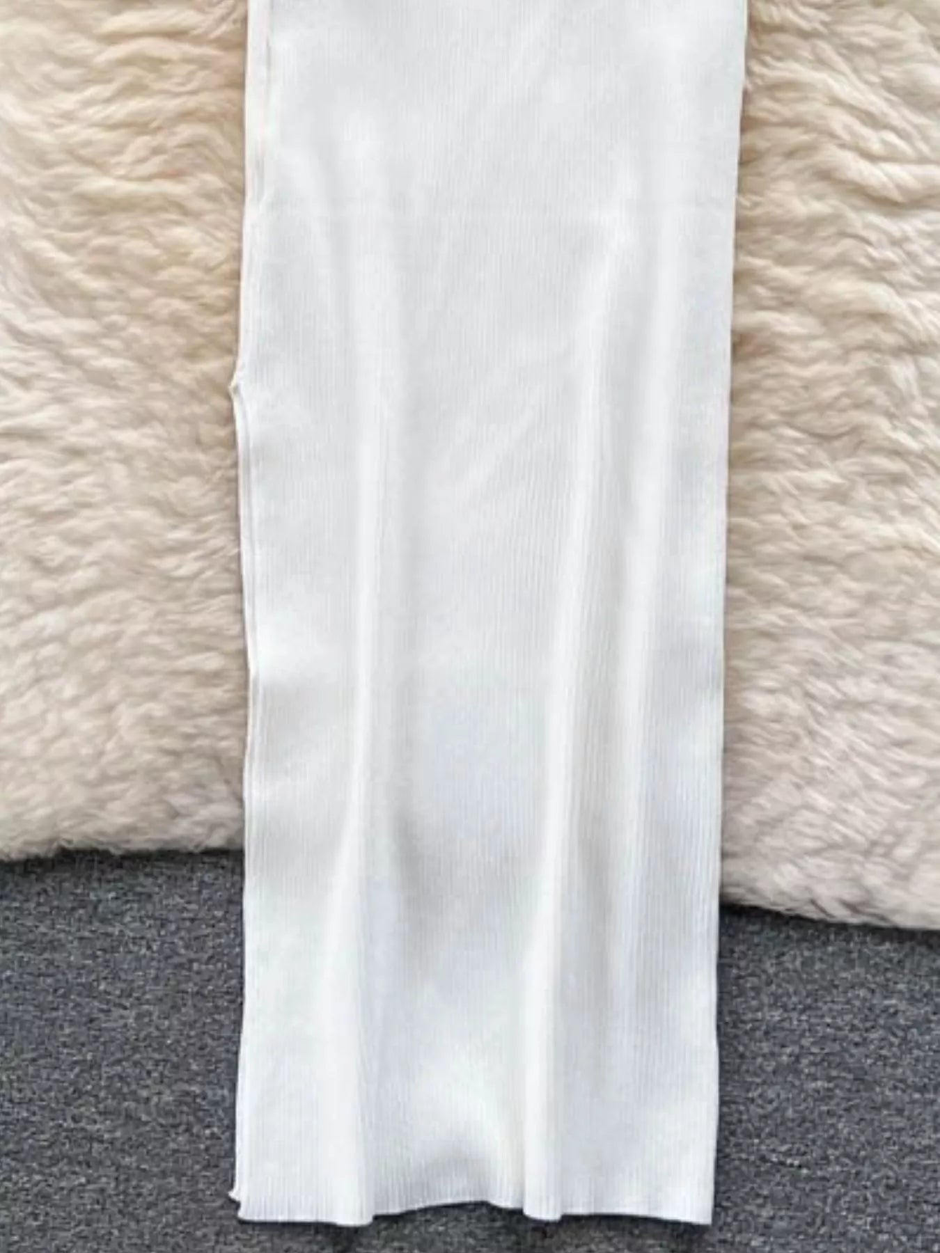 Lower skirt of white ribbed knit midi dress laid flat on soft rug