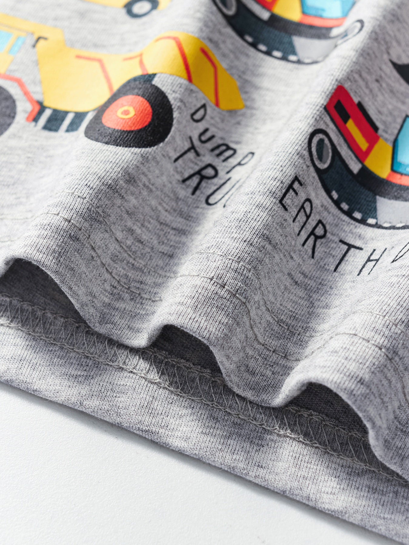 Close-up of the hem stitching and fabric texture on a light gray children's construction vehicle T-shirt