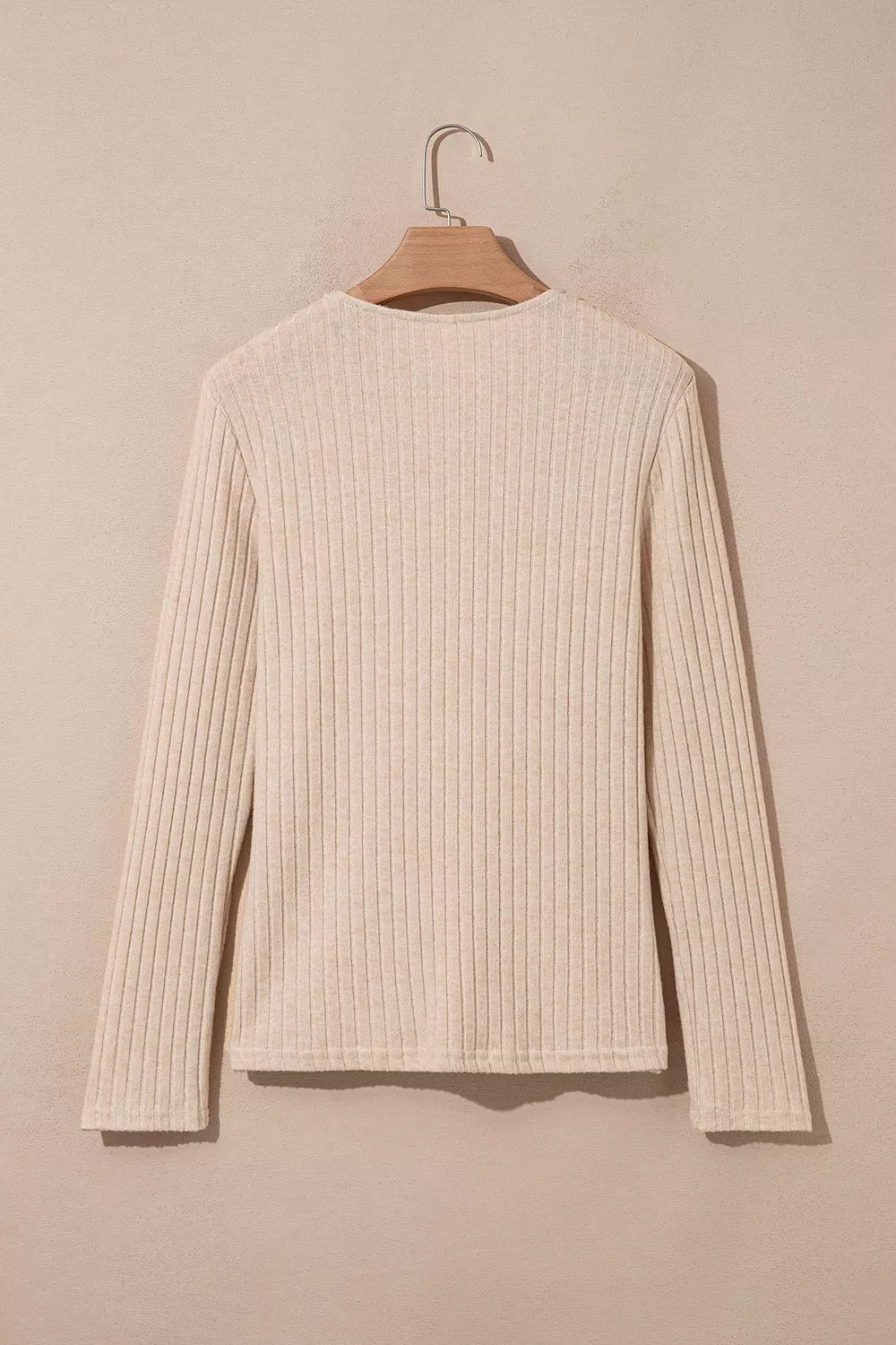 Cream ribbed long-sleeve top with a round neckline hanging on a wooden hanger