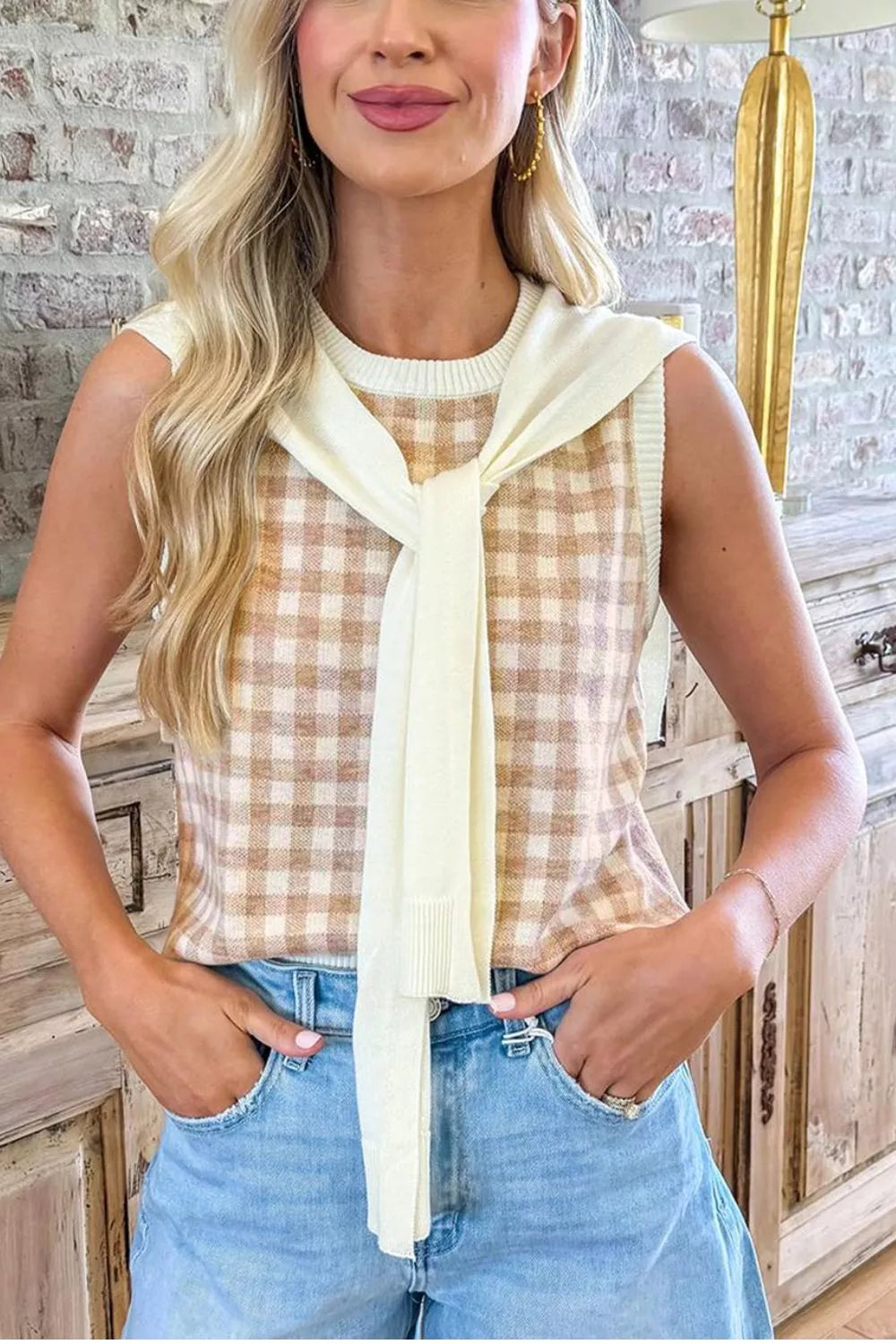 Close front view of a tan gingham knit sweater vest with a cream sweater draped over the shoulders
