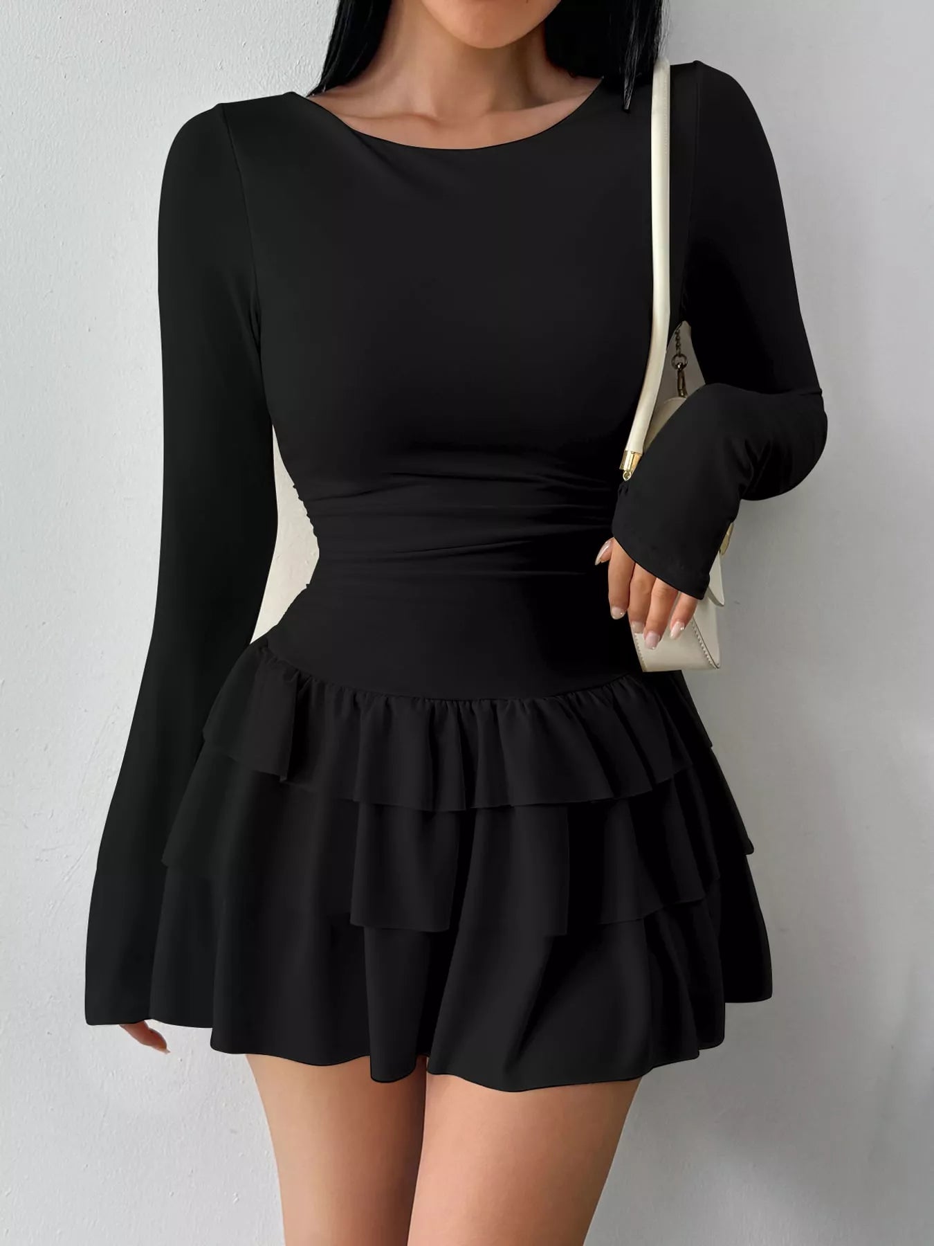 Black layered ruffle long sleeve mini dress worn front facing with a white shoulder bag