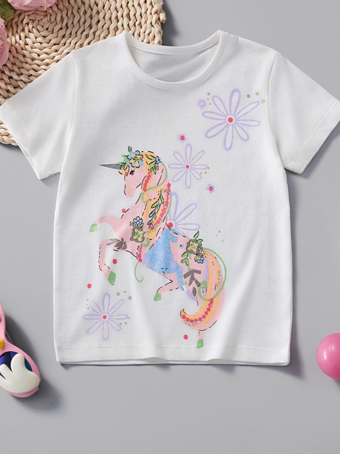 White children's short sleeve tee laid flat with a pink floral unicorn graphic