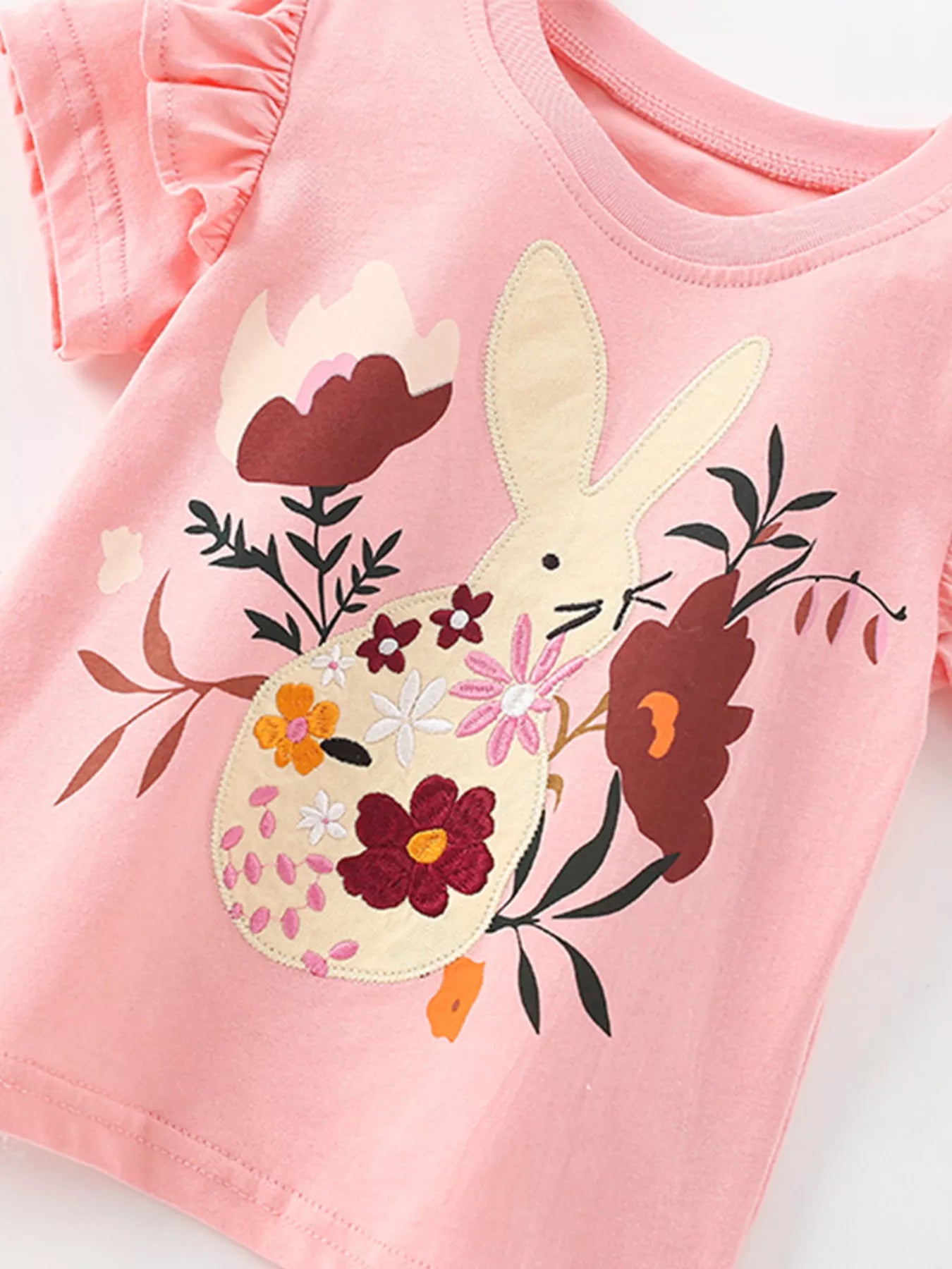 Angled close-up of cream bunny applique with colorful flowers on blush pink t-shirt
