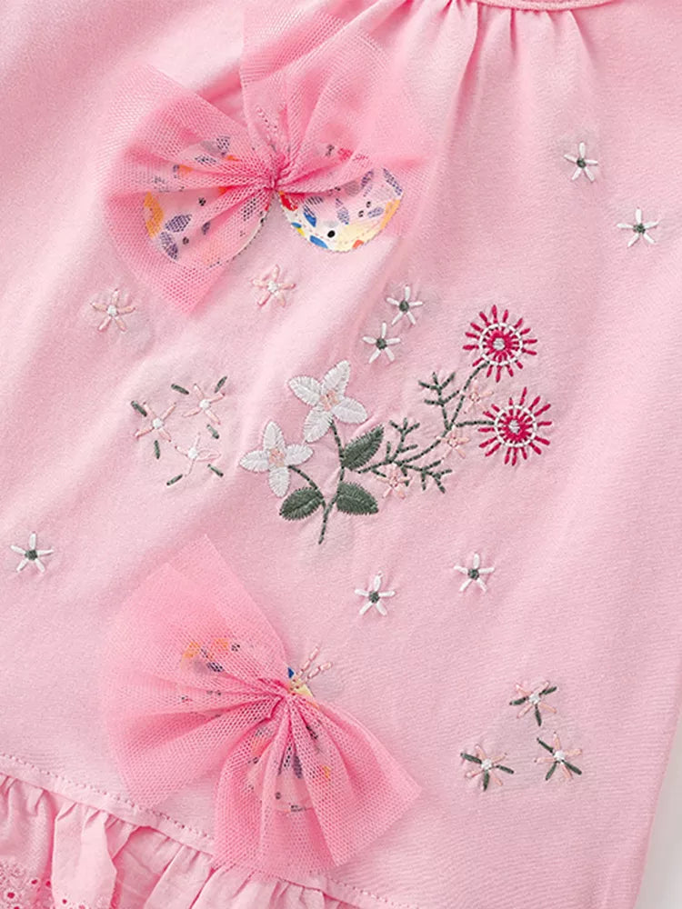 Detail view of pink tulle bows and floral embroidery on the front of a children's blush pink t-shirt