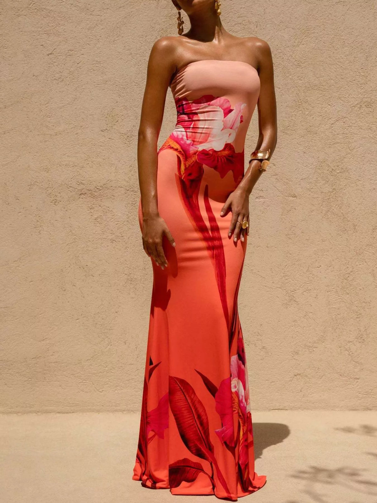 Model wearing strapless coral orange floral tube maxi dress, front view against beige wall