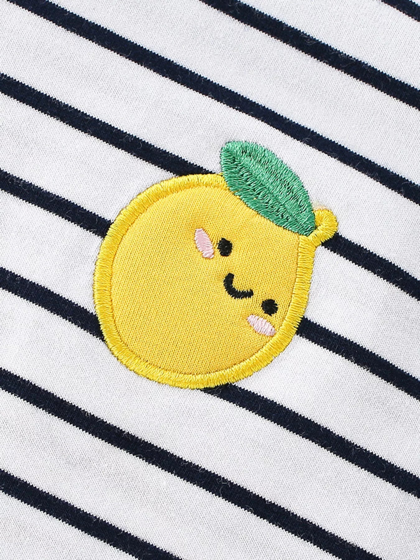 Close-up of the embroidered yellow lemon applique with green leaf on white navy striped fabric