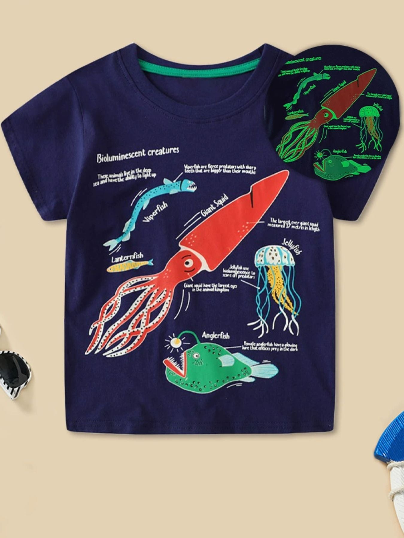 Dark navy children's t-shirt with colorful bioluminescent sea creatures print and glowing inset, front view